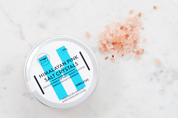 Pink rock salt crystals against a marble background with a tin to the side