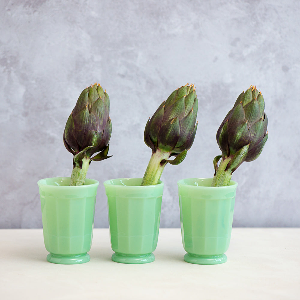 lifestyle photograph of three mosser glass jadeite tumblers in milk glass with artichokes vase